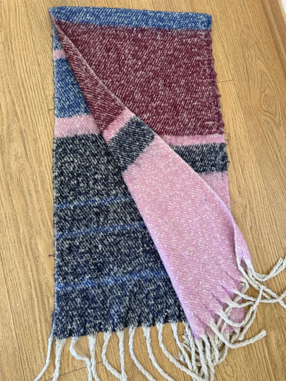 Bufanda tejida a rayas en tonos de rosa, bordó, azul y gris. Posee flecos en los extremos.