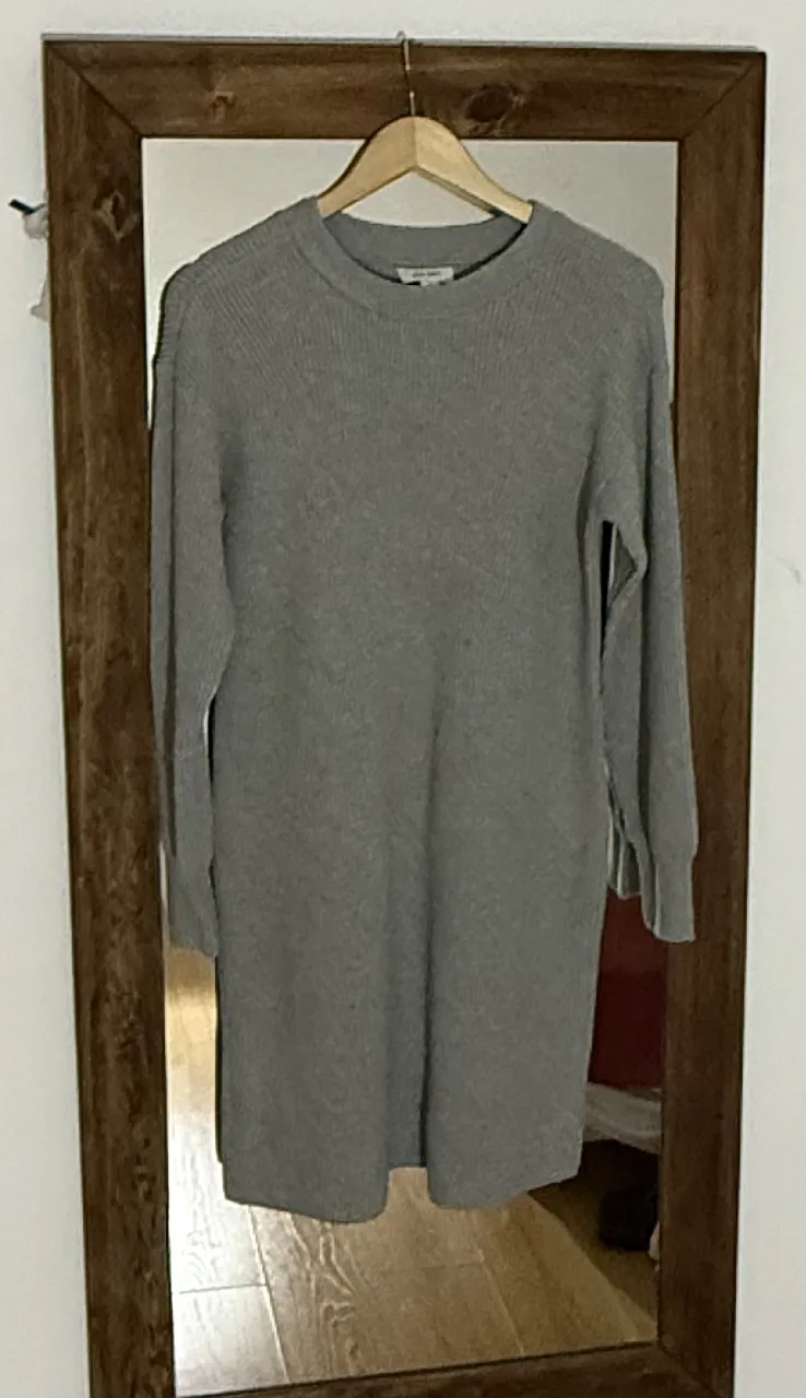 Vestido de tejido gris, largo hasta la rodilla, con mangas largas y cuello redondo. Ideal para un look casual y cómodo.