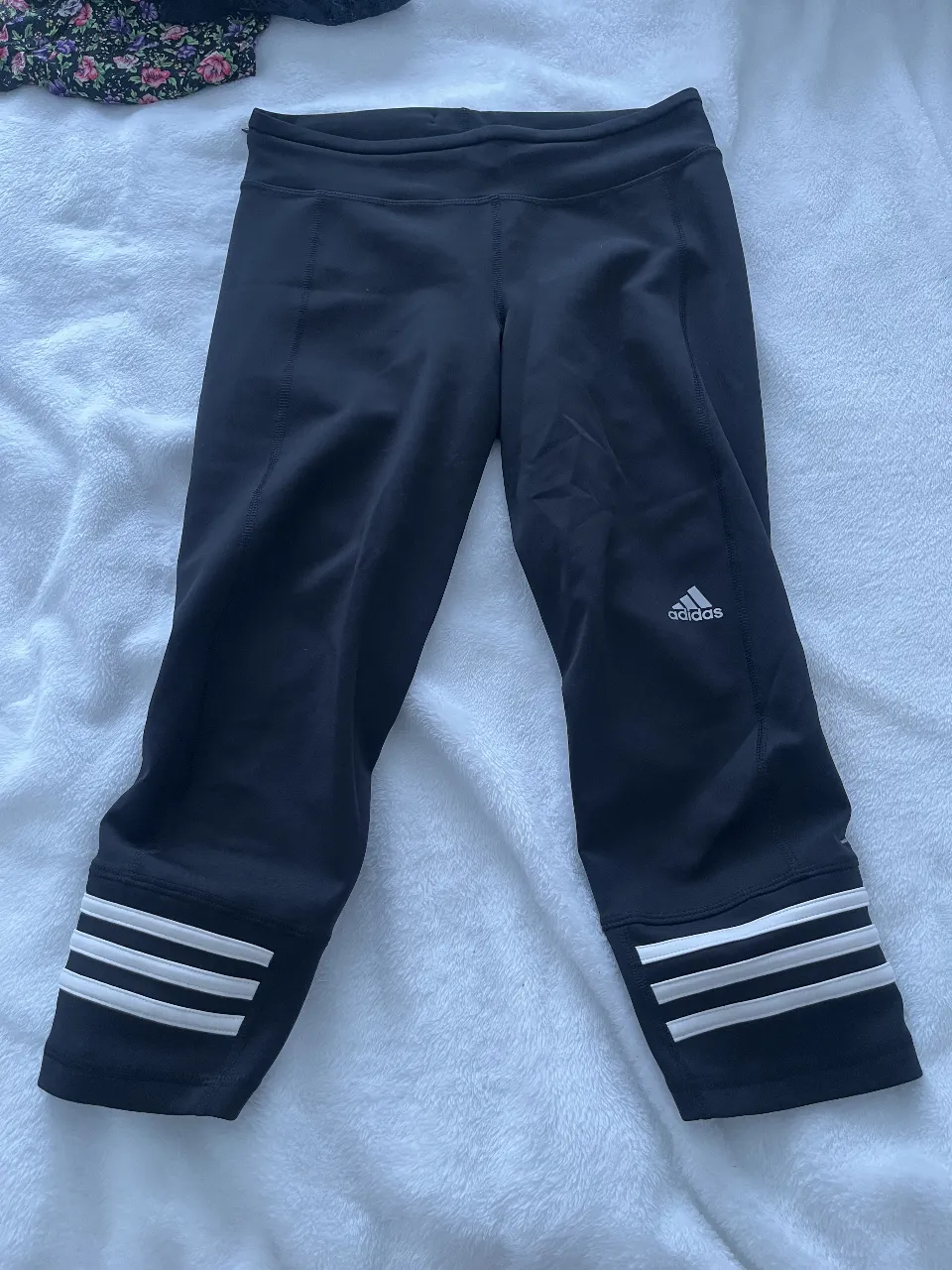 Calzas Adidas  negras, con las tres tiras clásicas en blanco . Logo de la marca en blanco. Ideal para running y entrenamiento.