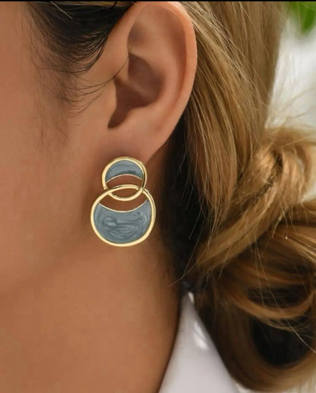Aros colgantes con diseño geométrico de dos círculos entrelazados, con detalles en dorado y esmalte azul. Ideales para darle un toque moderno y sofisticado a cualquier look.
