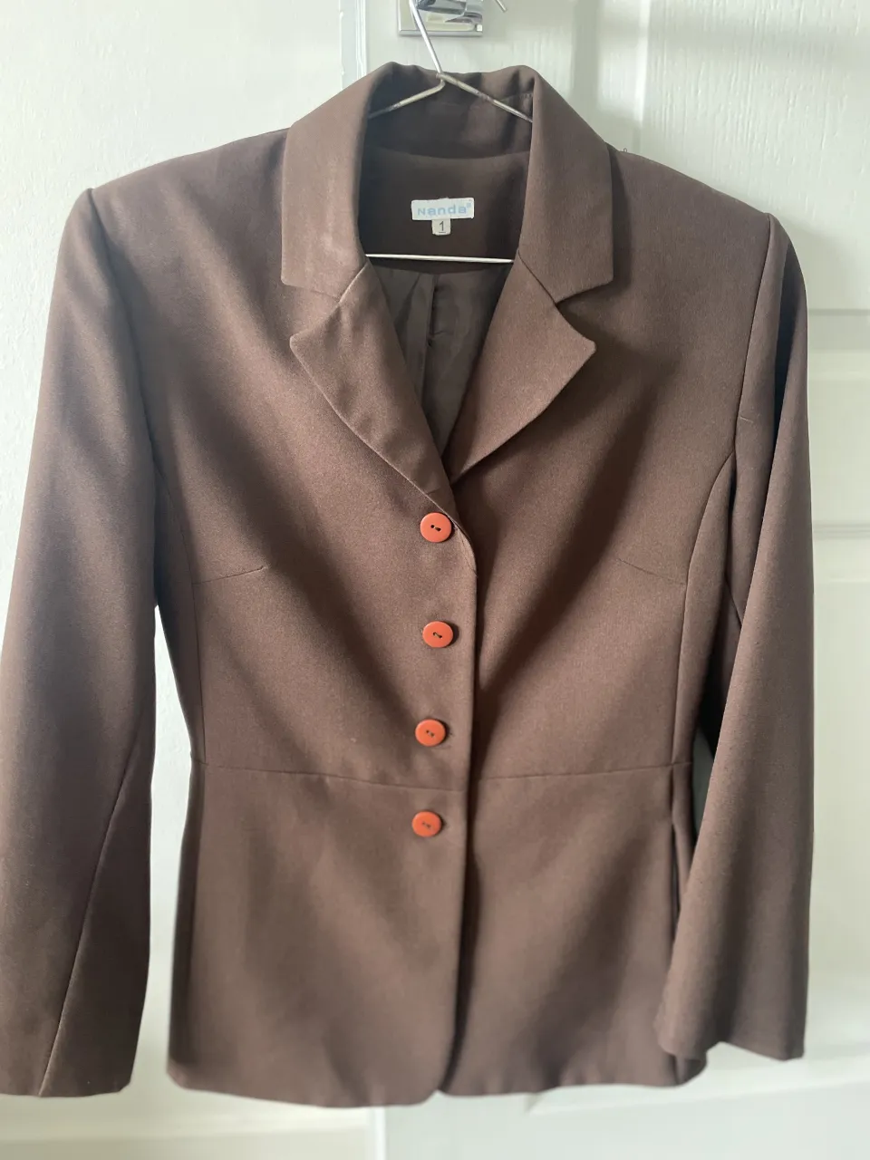 Blazer marrón de Nanda con tres botones naranjas al frente. Cuello solapa.