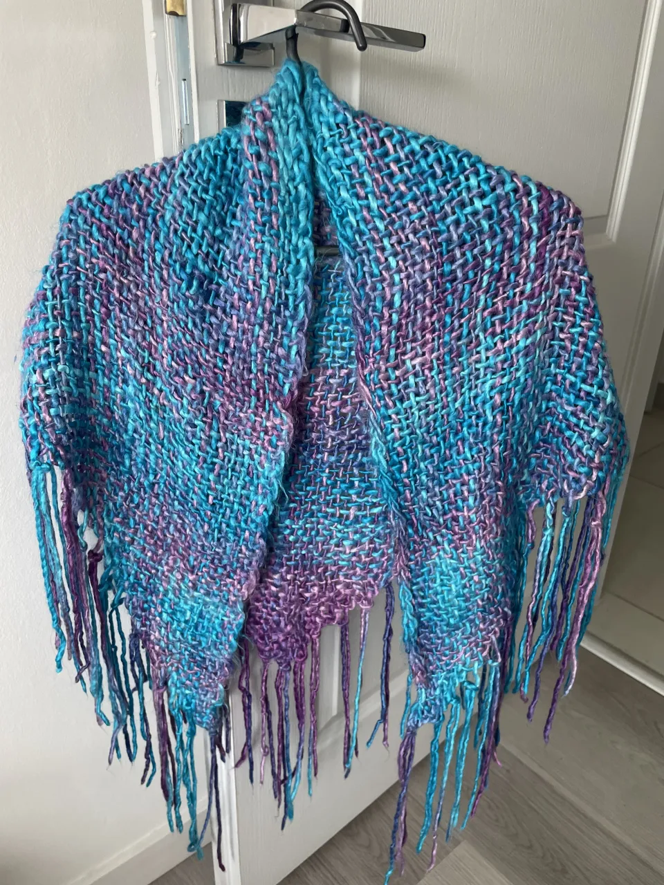 Chalina tejida con flecos largos. Presenta una trama de hilos en tonos de azul y violeta.