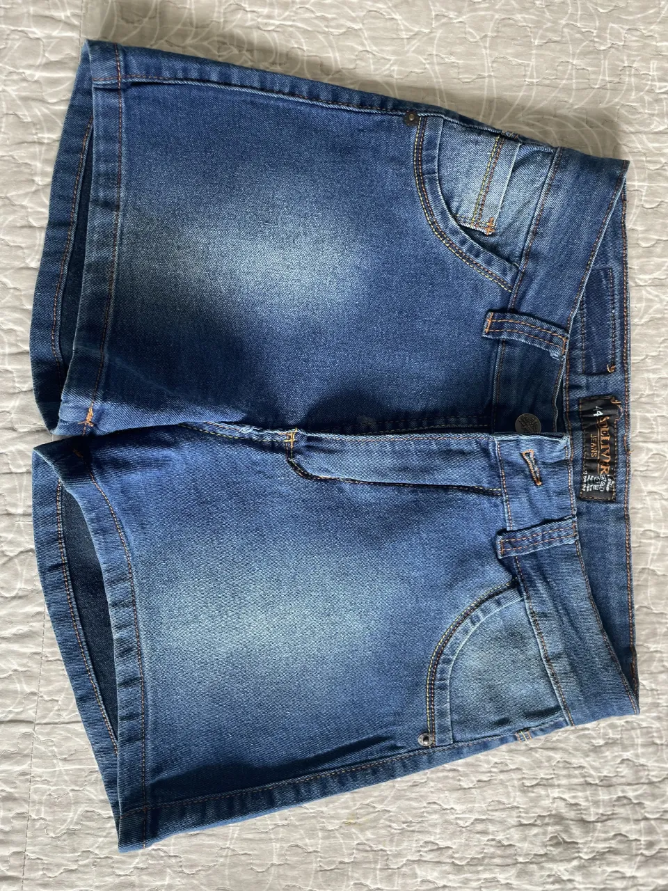 Shorts de jean azul con desgastes. Tienen bolsillos delanteros y traseros.