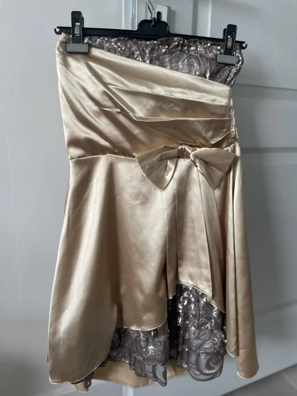 Vestido strapless dorado con detalles de lentejuelas plateadas en la parte superior y en el ruedo. Posee un lazo de tela en la cintura.