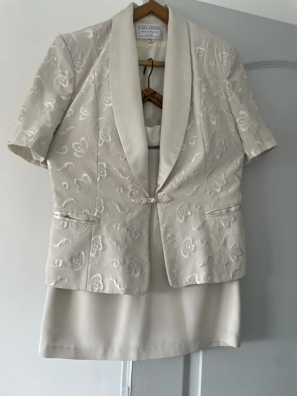 Conjunto de saco corto con bordados florales y falda lisa. El saco es de mangas cortas y tiene cuello solapa satinado. La falda es recta y de largo hasta la rodilla.