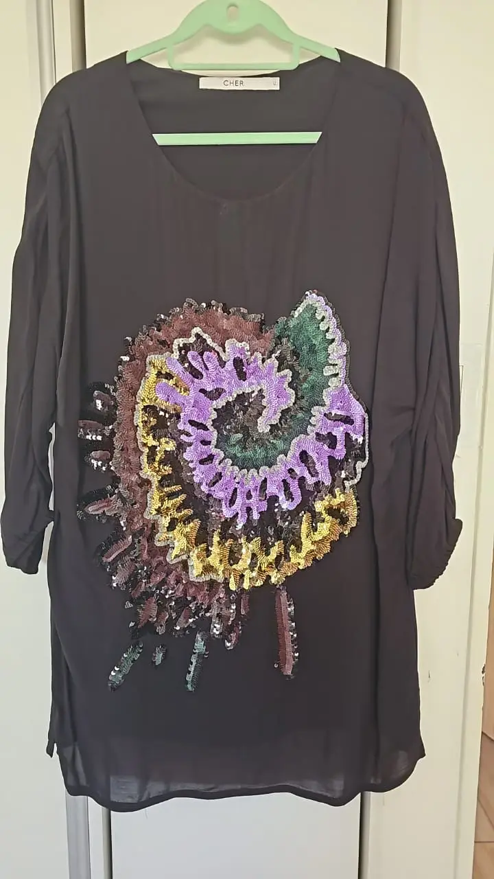 Blusa negra de Cher con aplique floral en lentejuelas. Ideal para una salida o evento especial.