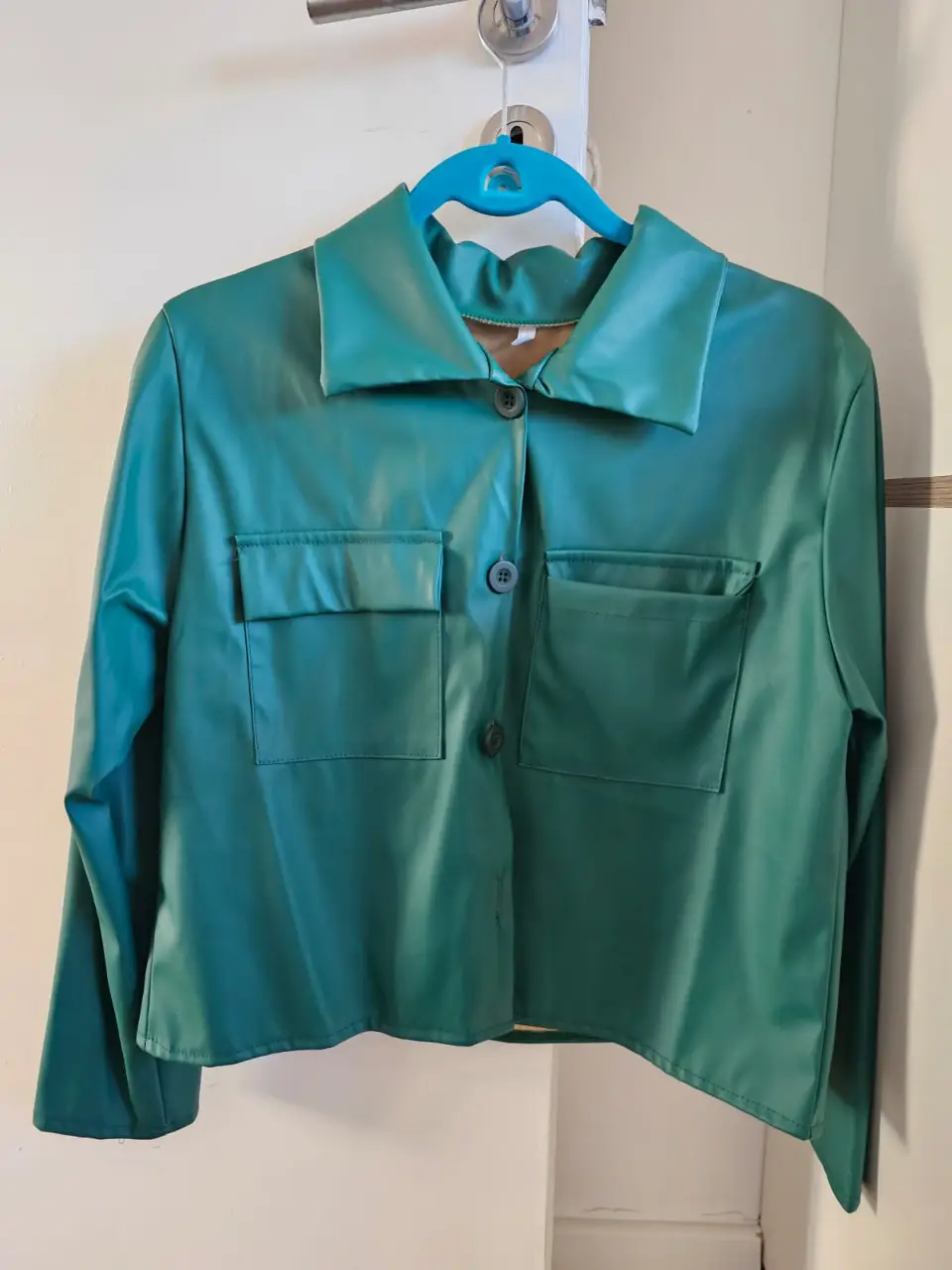 Chaqueta estilo biker de cuero sintético en color verde. Posee dos bolsillos delanteros con solapa y botones, y cierre frontal con botones. Ideal para un look moderno y audaz. hombro 43cm sisa 51cm largo manga 55cm largo chaqueta 54cm
