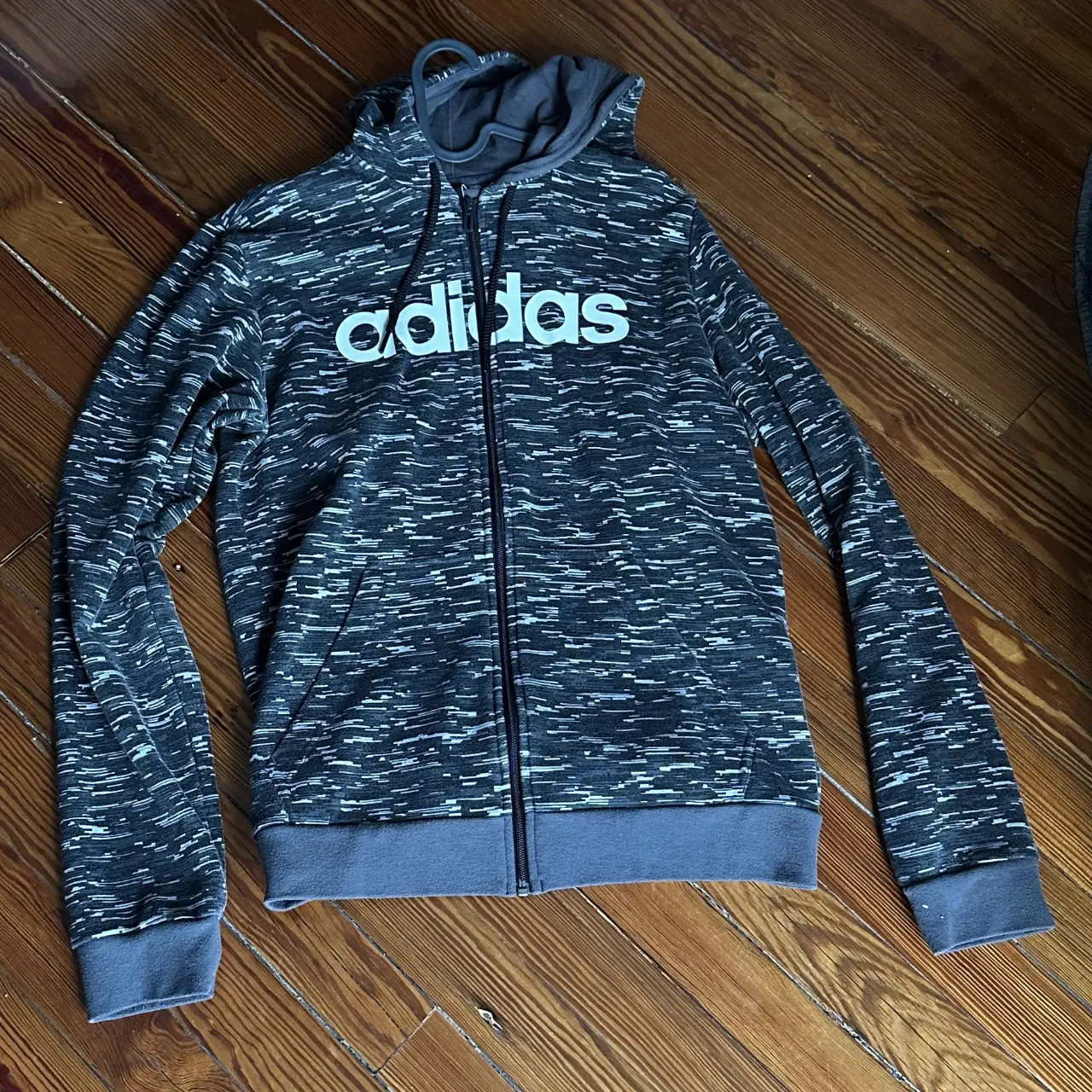 Buzo Adidas con cierre, de color gris con detalles en blanco. Ideal para un look deportivo y casual.