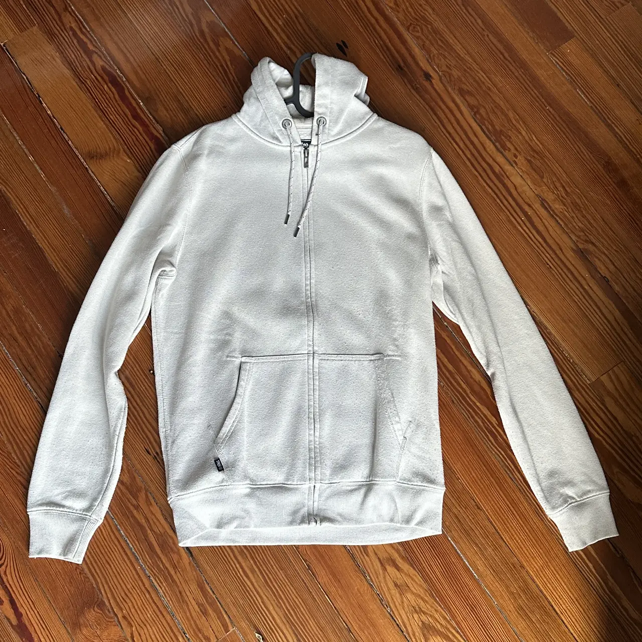 Buzo con cierre blanco, con capucha y bolsillo tipo canguro. Ideal para un look casual y cómodo.