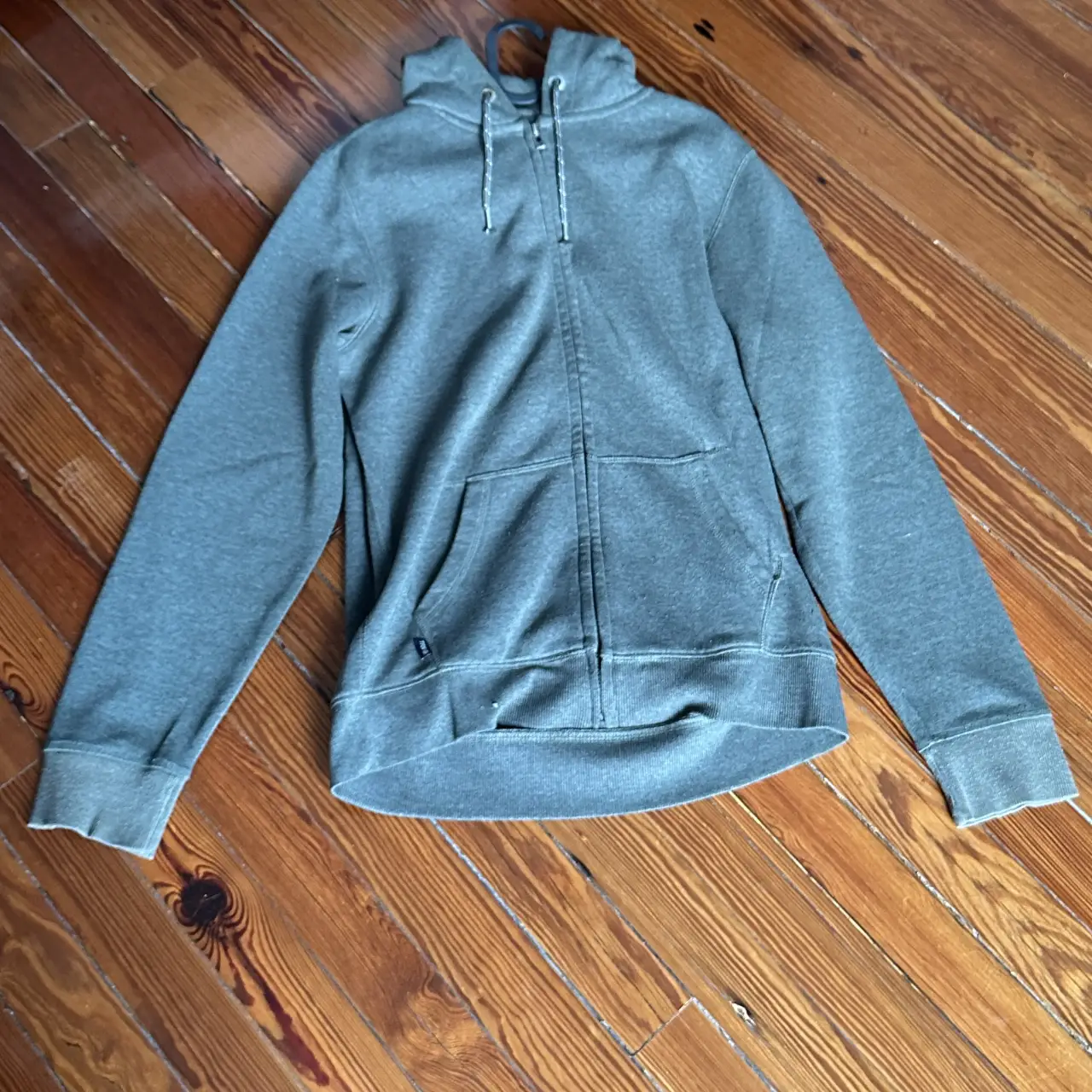 Buzo con cierre gris, con capucha y bolsillo tipo canguro. Ideal para un look casual y cómodo.