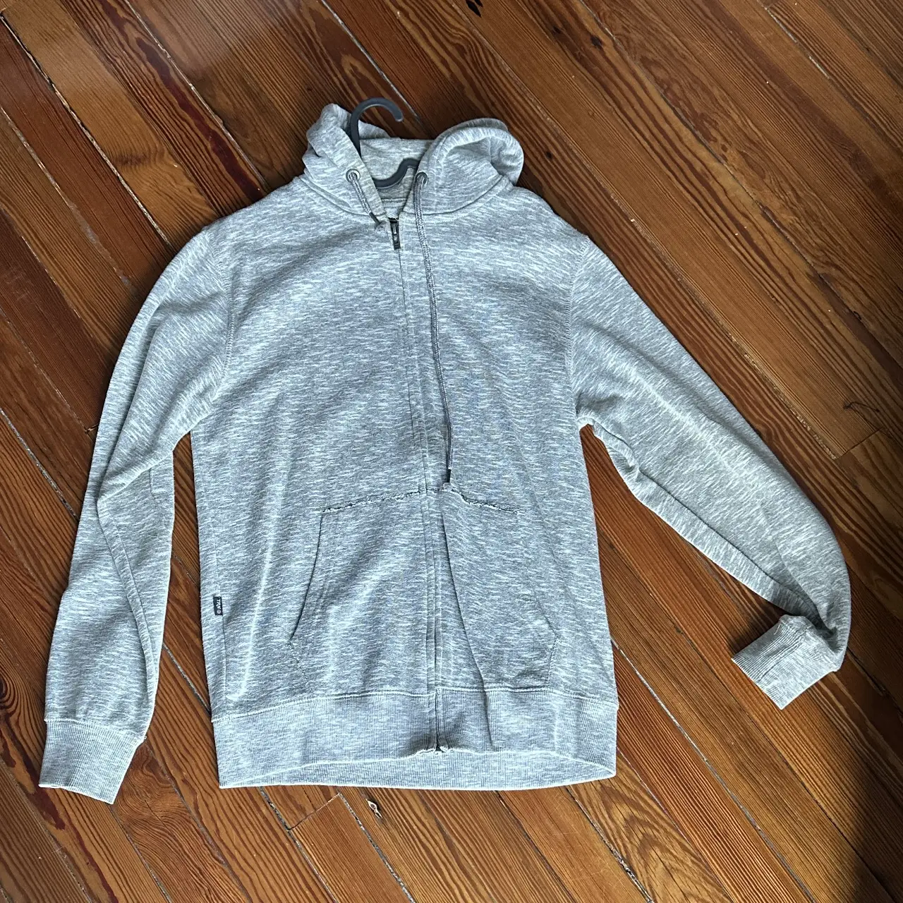 Buzo con cierre gris, con capucha y bolsillos. Ideal para un look casual y cómodo.