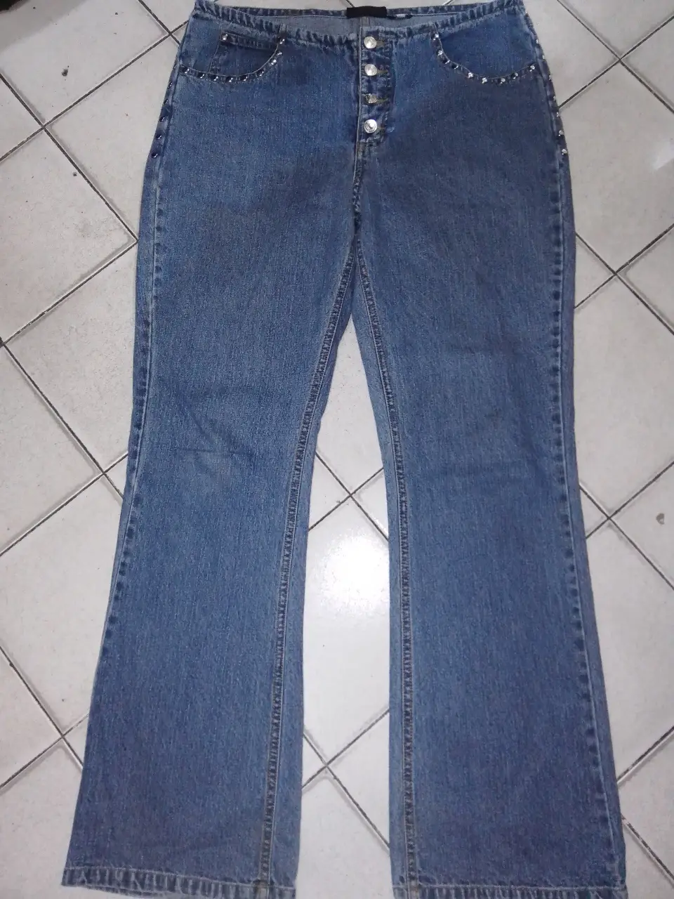 Jeans de mujer tiro alto, con botones y detalles de tachas en los bolsillos y cintura. Corte acampanado, ideal para un look Y2K.