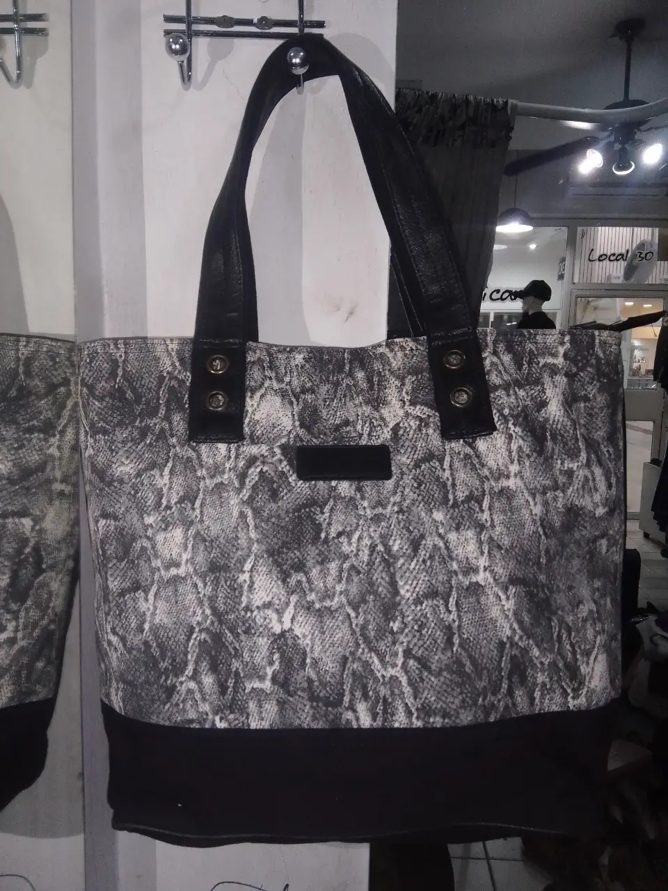 Bolso tote con estampado de piel de serpiente en tonos grises y negros. Detalles en negro liso en la base y las asas. Ideal para un look casual y moderno.