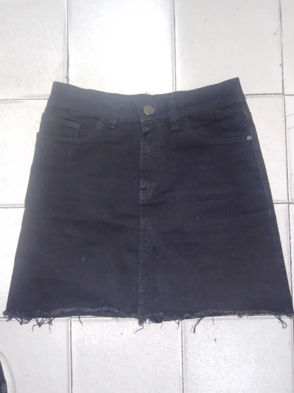 Pollera larga de jean negra, con un corte recto y un detalle de flecos en el borde inferior. Ideal para un look casual y moderno.