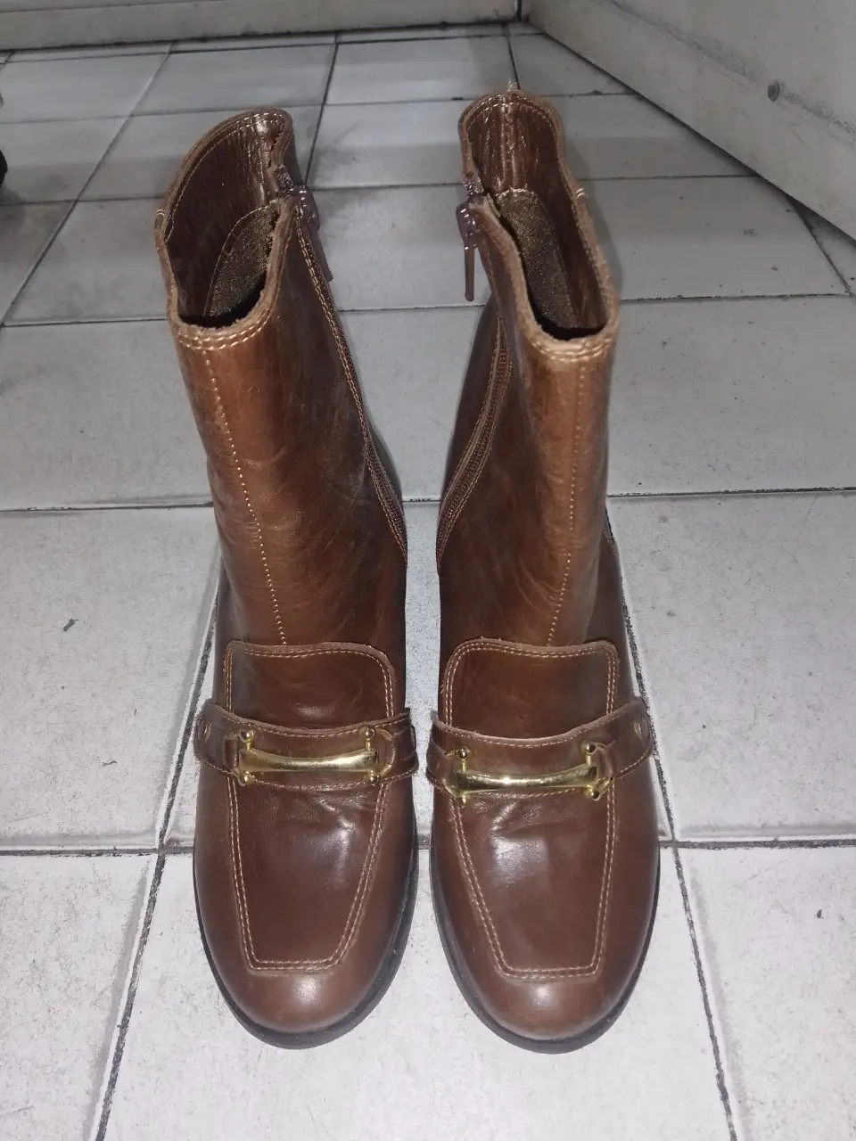Botas de caña alta de cuero marrón con detalles dorados en la parte delantera. Cierre lateral con cremallera y taco ancho.