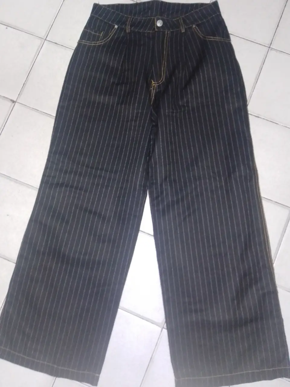 Pantalón sastrero a rayas verticales en color negro con detalles amarillos. Corte recto y tiro alto, ideal para un look elegante y moderno.
