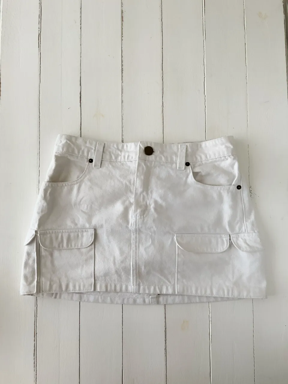 Pollera corta blanca con bolsillos cargo. Tiene un parche de cuero con el logo de la marca en la parte trasera.