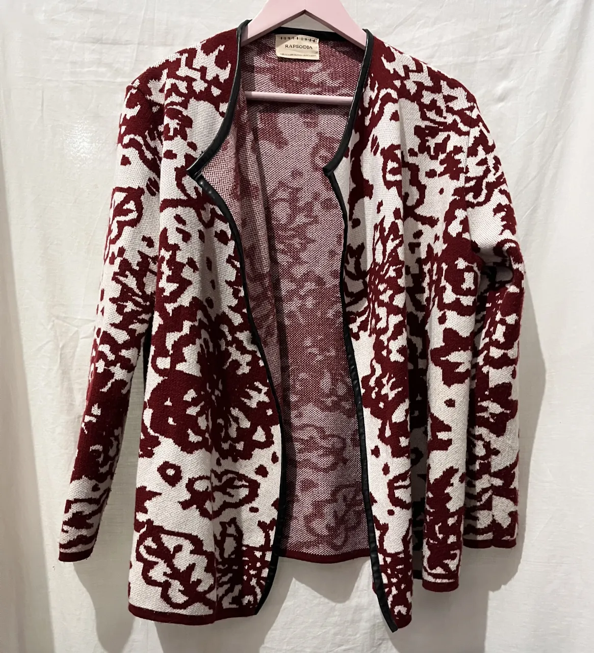 Cardigan tejido con estampa abstracta en tonos blanco y bordo. Posee cuello y puños con detalle de ecocuero negro.