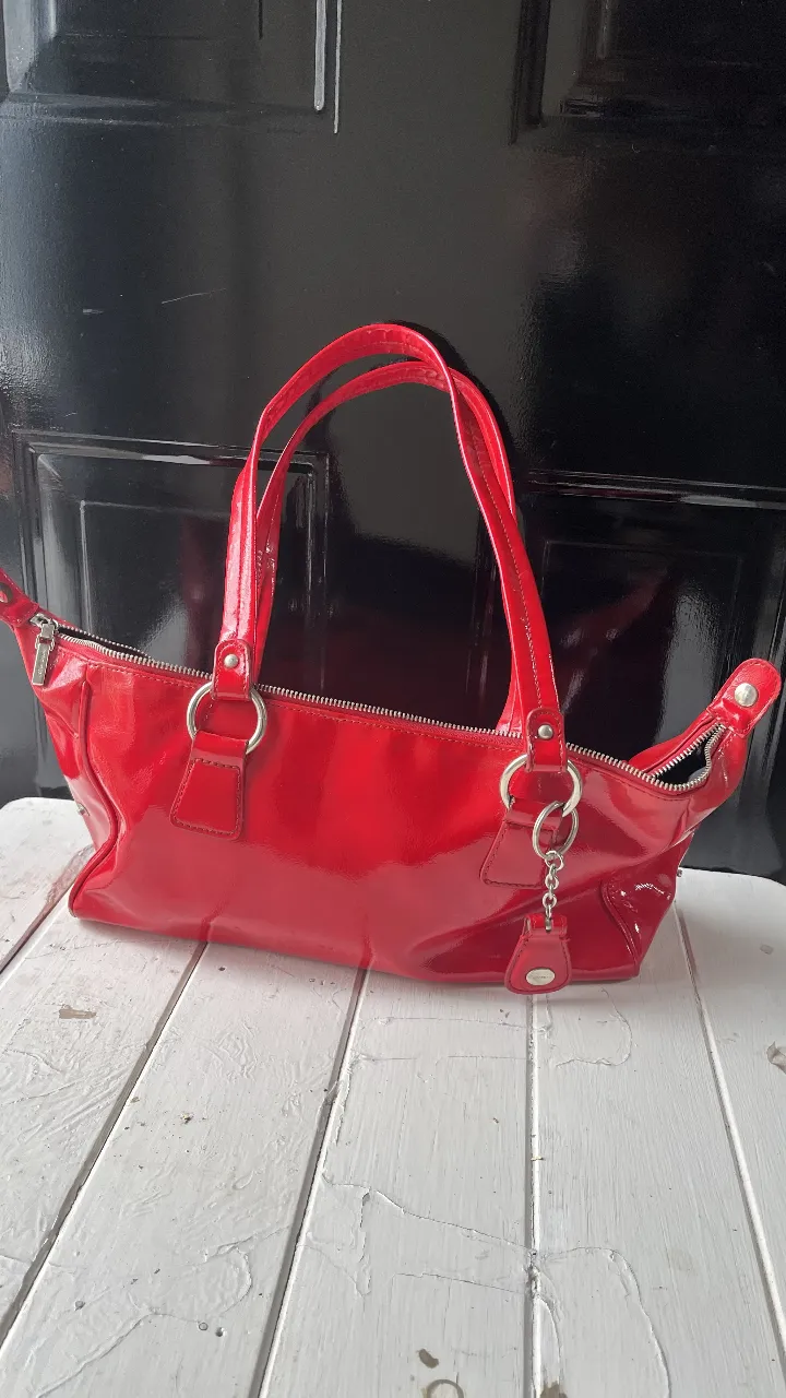 Cartera roja de charol, con manijas cortas y detalles plateados. Ideal para un look elegante y moderno. detalles importantes de la cartera de un lateral unas manchas negras probé sacarlo y no sale capas ustedes si y el cierre no cierra no intente foszar su cierre para no romperlo un especialista si sabe esos son los detalles es hermosa la cartera 🫶💞❤️ otro detalle se le bajó el valor dos veses para que su arreglo sea más fácil 👀📌