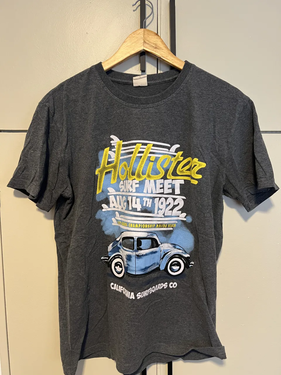 Remera gris oscuro de manga corta con estampa vintage de un auto y "Hollister Surf Meet Aug 14th 1922" en la parte delantera. Ideal para un look casual y relajado.
largo a hombro: 65
ancho axila a axila: 48
mangas: 20