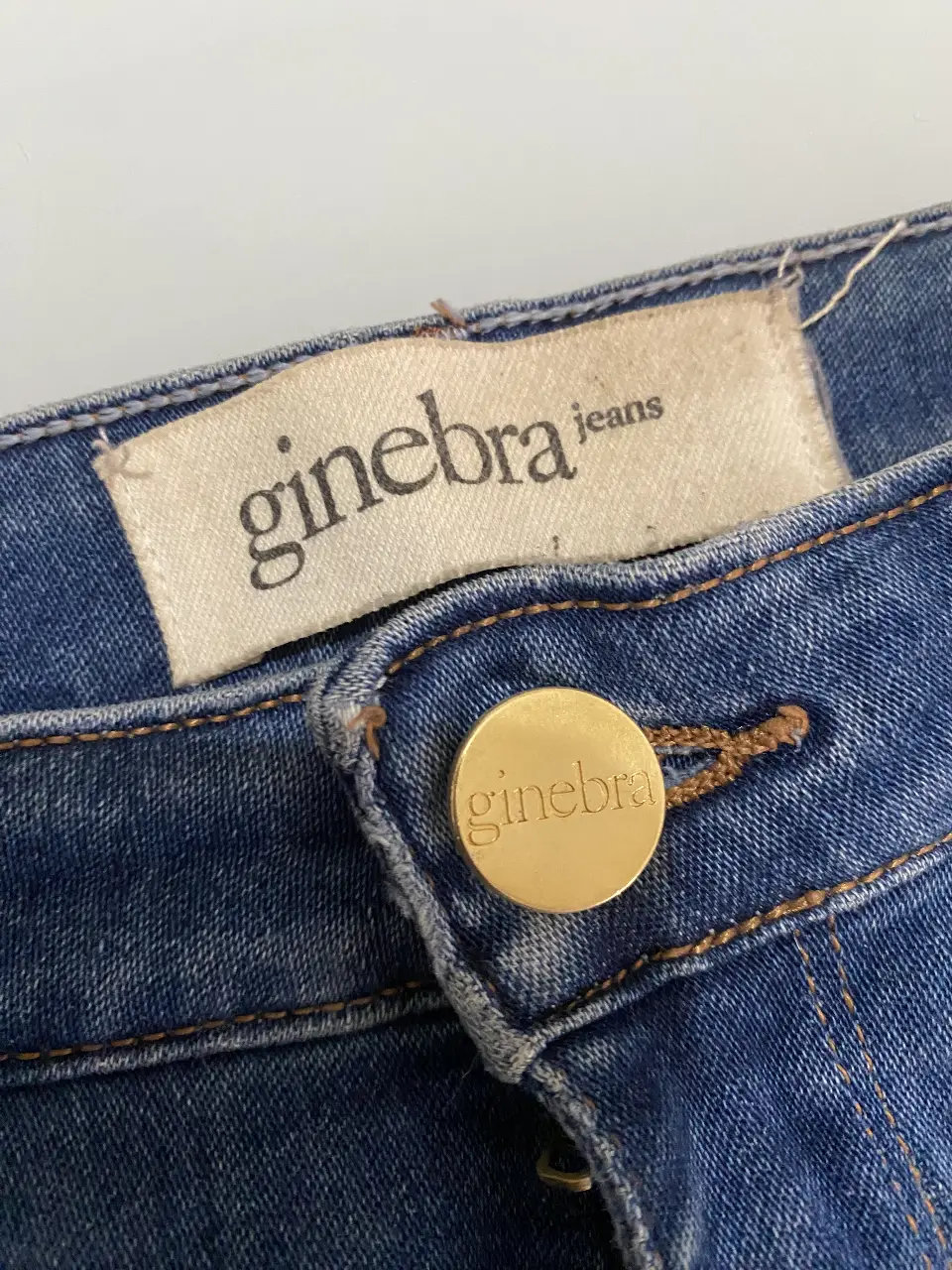 Jeans de mujer Ginebra, tiro medio, corte recto con aberturas en los bajos. Talle 38. Jeans de denim azul con detalles dorados en el botón y etiqueta de la marca.