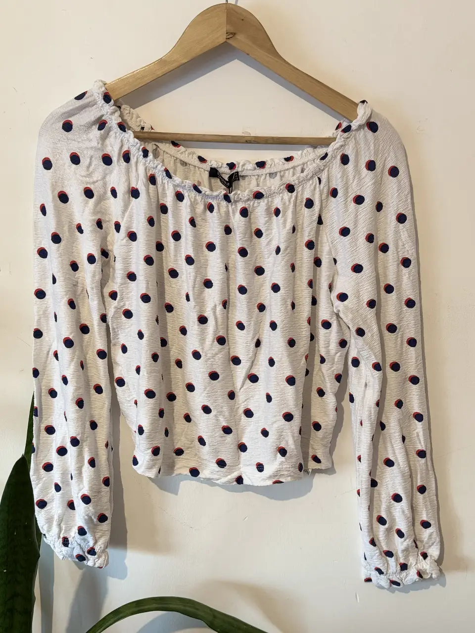 Blusa Bershka blanca con lunares azules y detalles rojos. Manga larga con puños elastizados y cuello redondo. Ideal para un look casual y moderno.