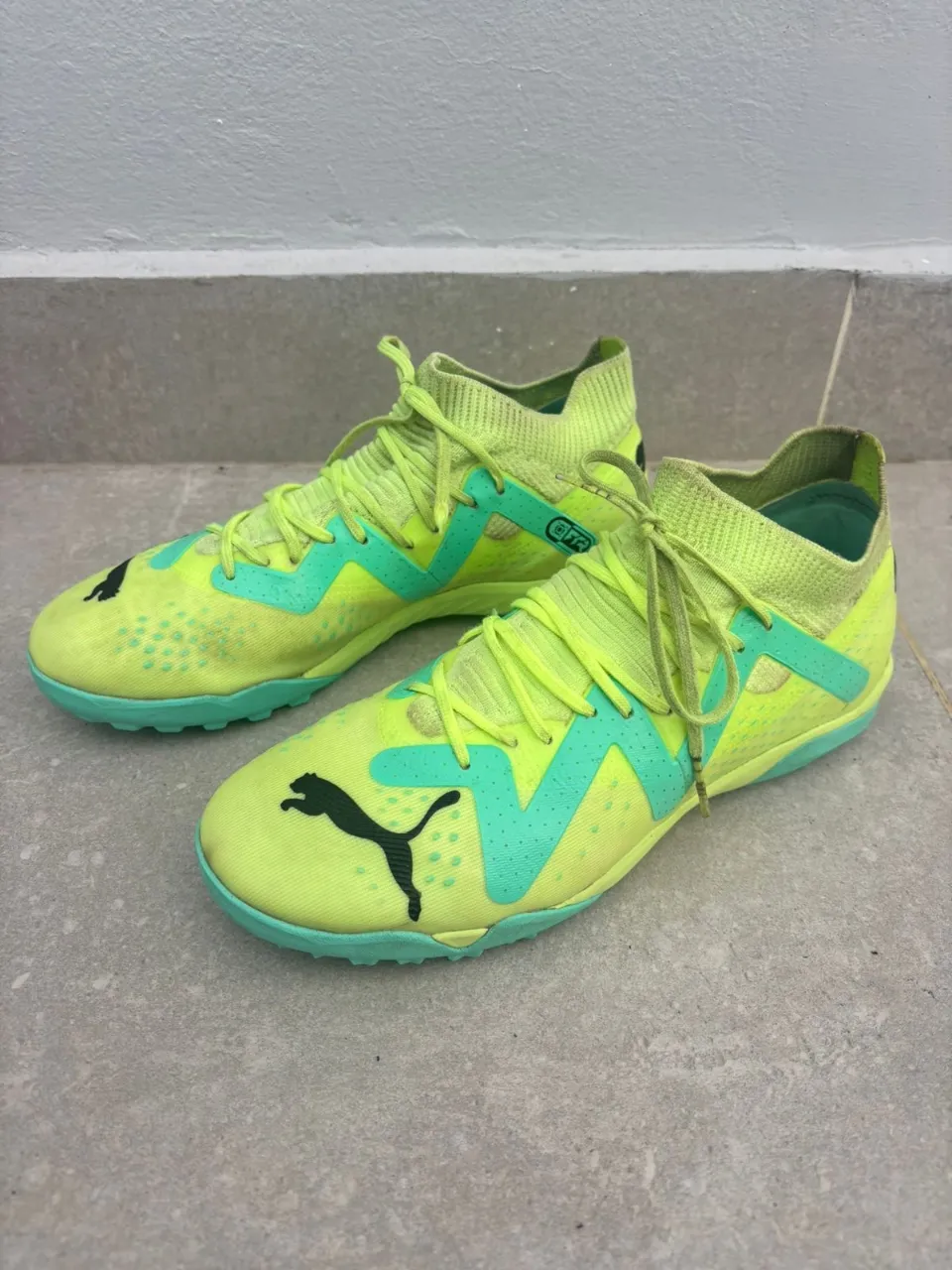 Zapatillas deportivas de color amarillo neón con detalles en verde menta. Presentan el logo de Puma en negro en los laterales y en la puntera. La suela es de goma con un diseño de tacos pronunciados.