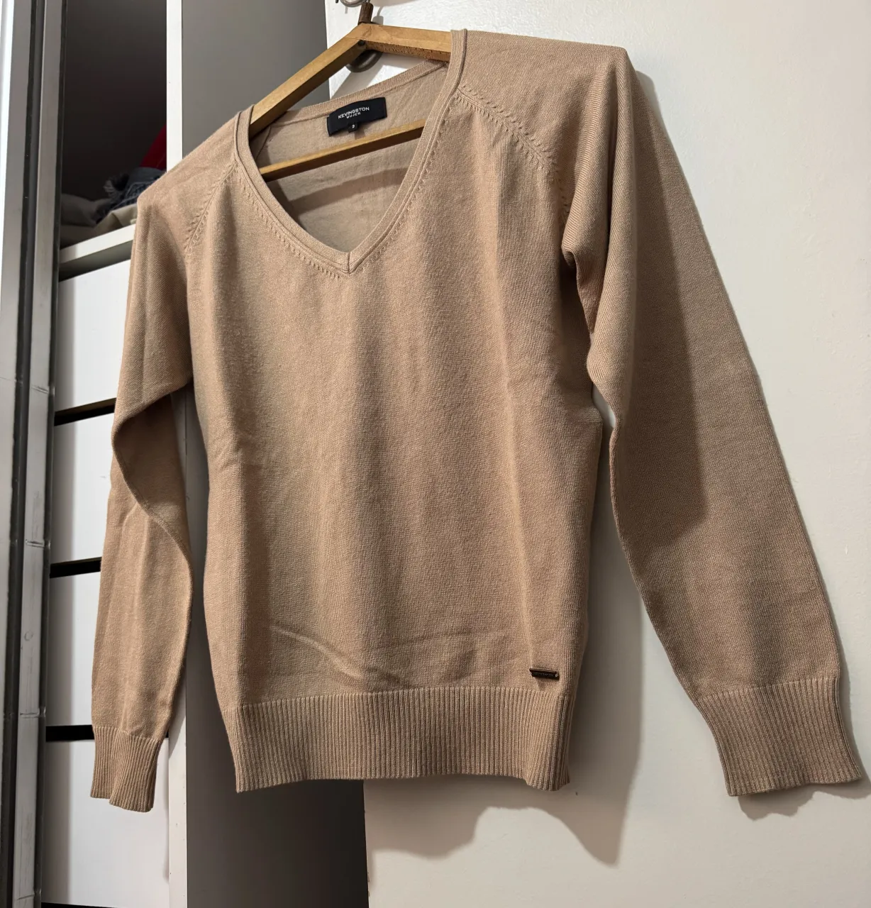 Sweater de tejido de punto color beige, con cuello en V y mangas largas. Posee puños y cintura tejidos.