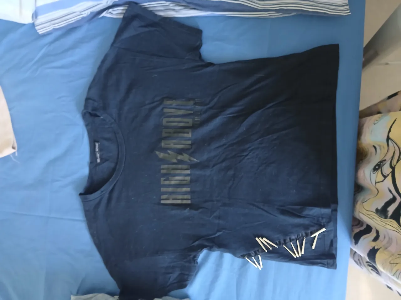 Remera negra con estampa "HIGH ABOVE" y un rayo en el centro. Tiene detalles de costura en la parte inferior.