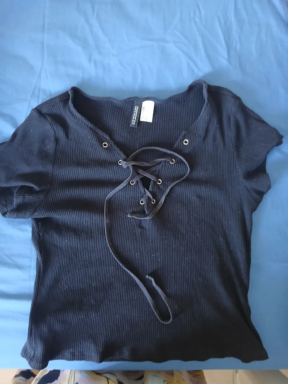 Remera negra de manga corta con escote en V y cordones para atar. Posee detalles acanalados.