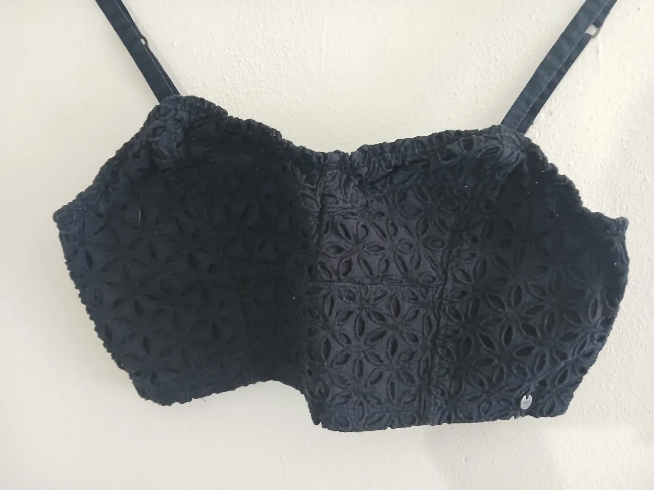 Top negro de encaje con tiras finas y detalle de fruncido en la parte inferior. Posee un diseño floral calado.