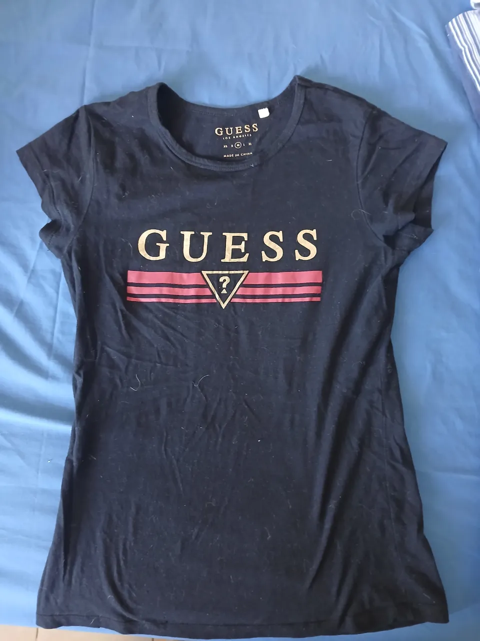 Remera negra de manga corta con estampa del logo "GUESS" en dorado y rojo.
