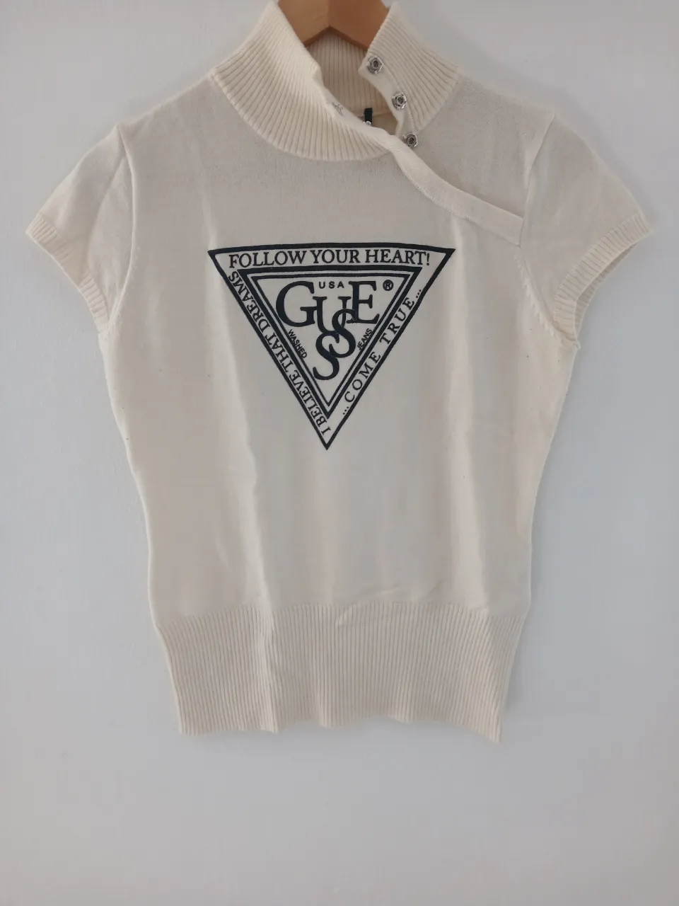 Remera de cuello alto con mangas cortas y estampa triangular de la marca Guess. Color blanco roto.
