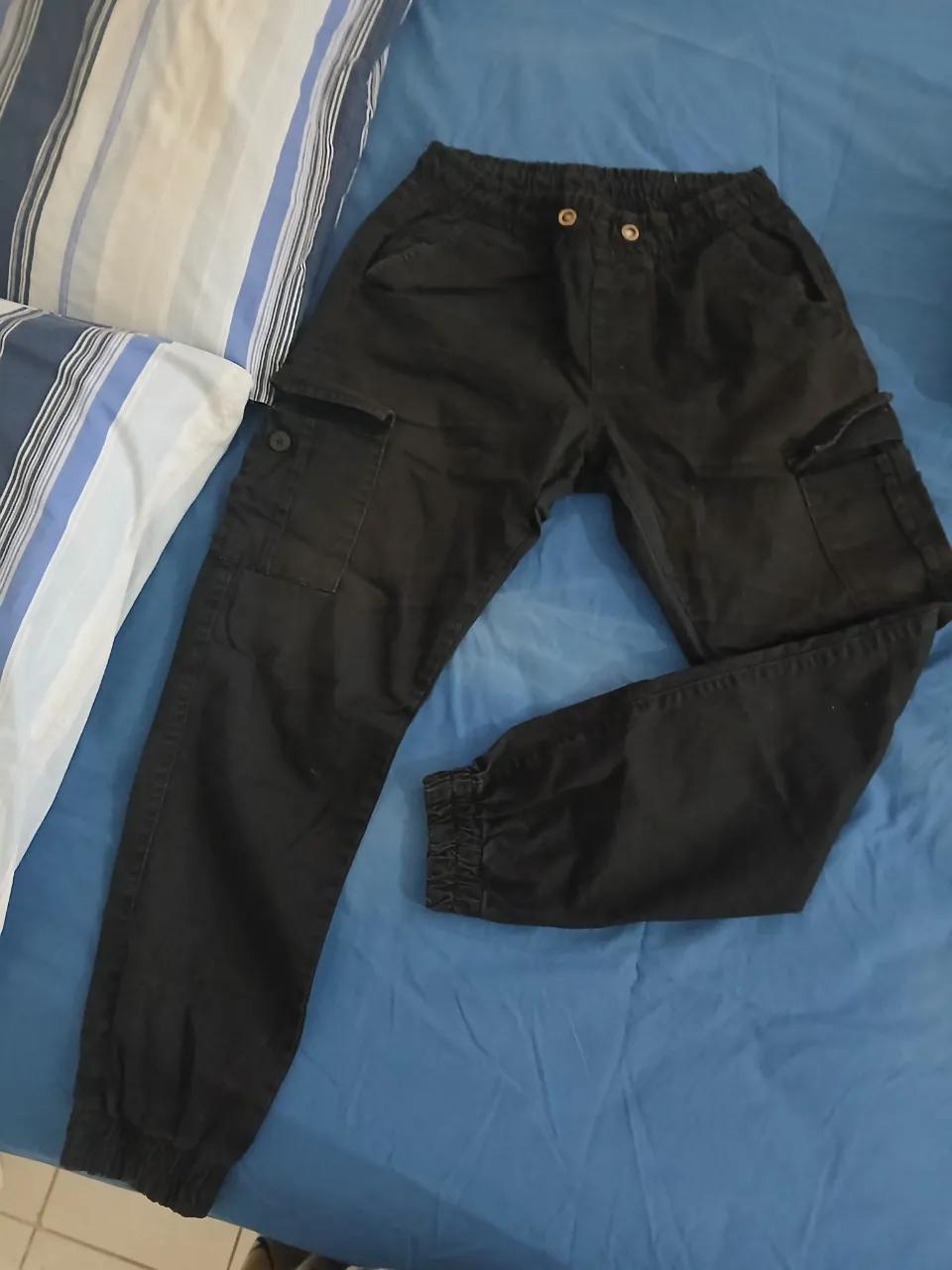 Pantalón cargo negro con bolsillos laterales y elástico en la cintura y tobillos. Posee cordones en la cintura para ajustar.