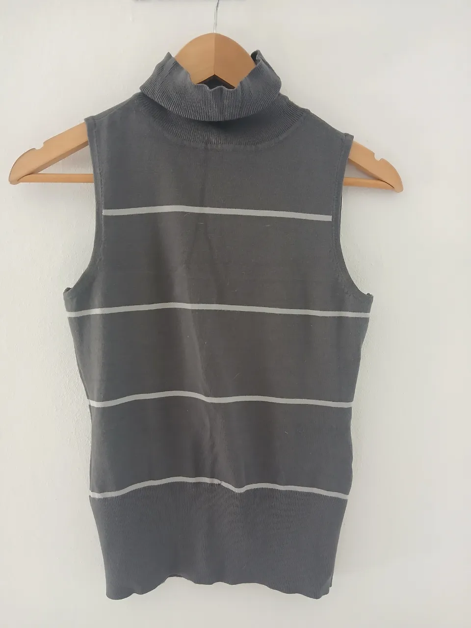 Remera de cuello alto sin mangas, de tejido de punto, con rayas horizontales finas en gris claro sobre fondo gris oscuro.