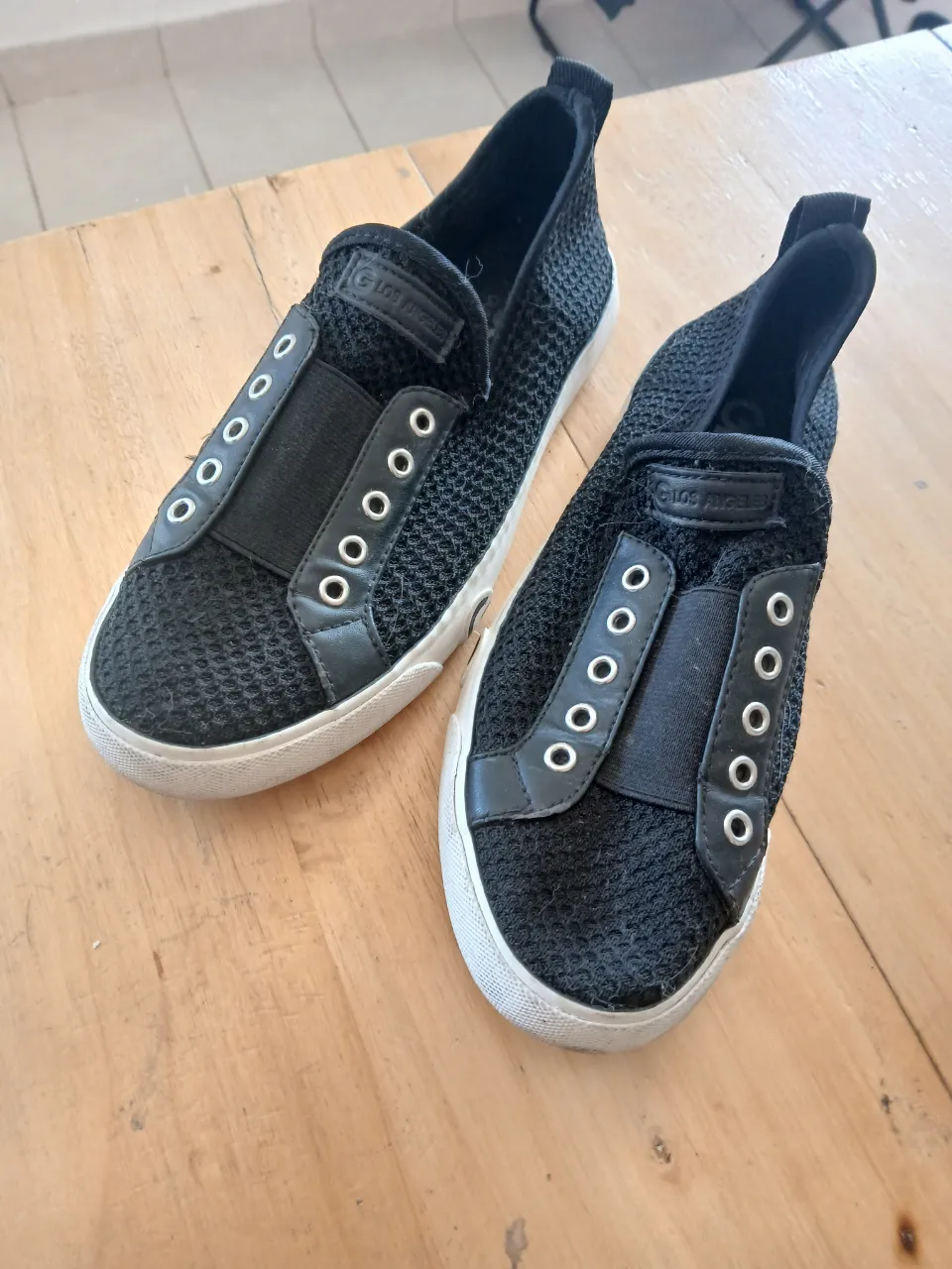 Zapatillas urbanas negras sin cordones, con detalles de ojales y suela blanca.