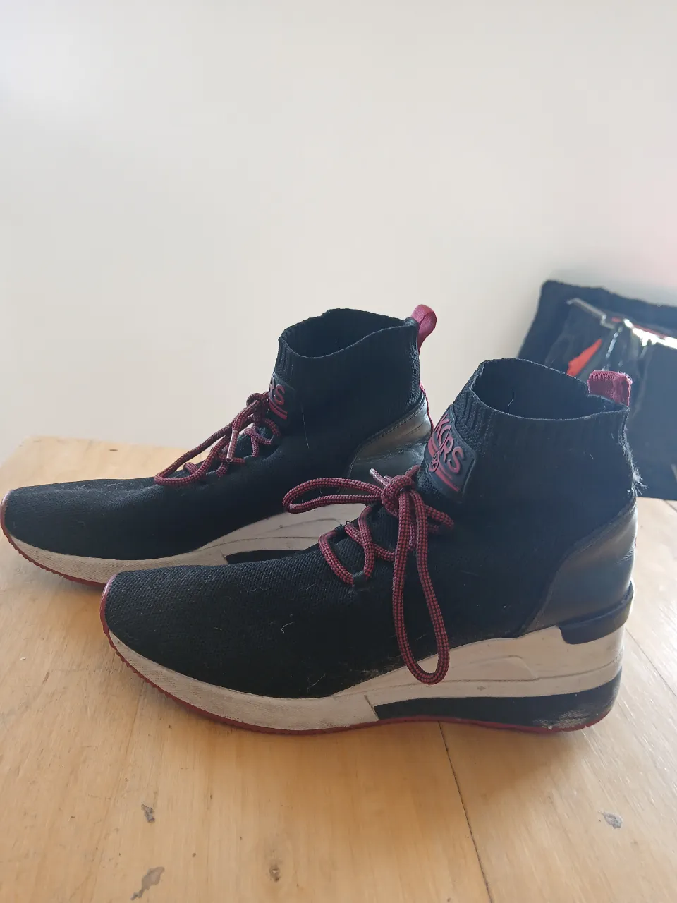 Zapatillas deportivas negras con cordones rojos y detalles en blanco y bordó. La lengüeta y el cuello son de tela elastizada.