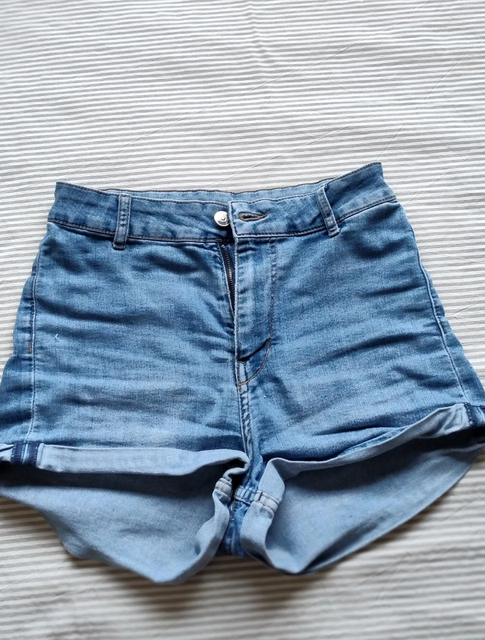 Shorts de jean tiro alto con roturas y dobladillo en la parte inferior. Cierre de cremallera y botón.