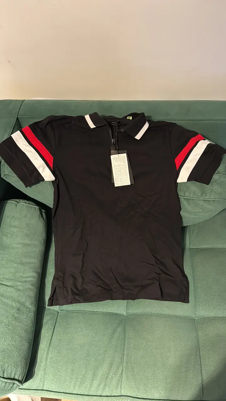 Remera de hombre negra con detalles en rojo y blanco en las mangas. Cuello polo con cierre y etiqueta. Ideal para un look casual y deportivo.