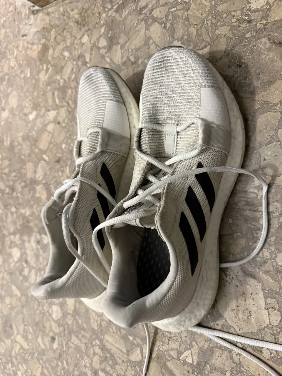 Zapatillas Adidas blancas con detalles en negro. Tienen un diseño deportivo y moderno, ideales para running o uso diario. Su suela es de color blanco con detalles en la base.