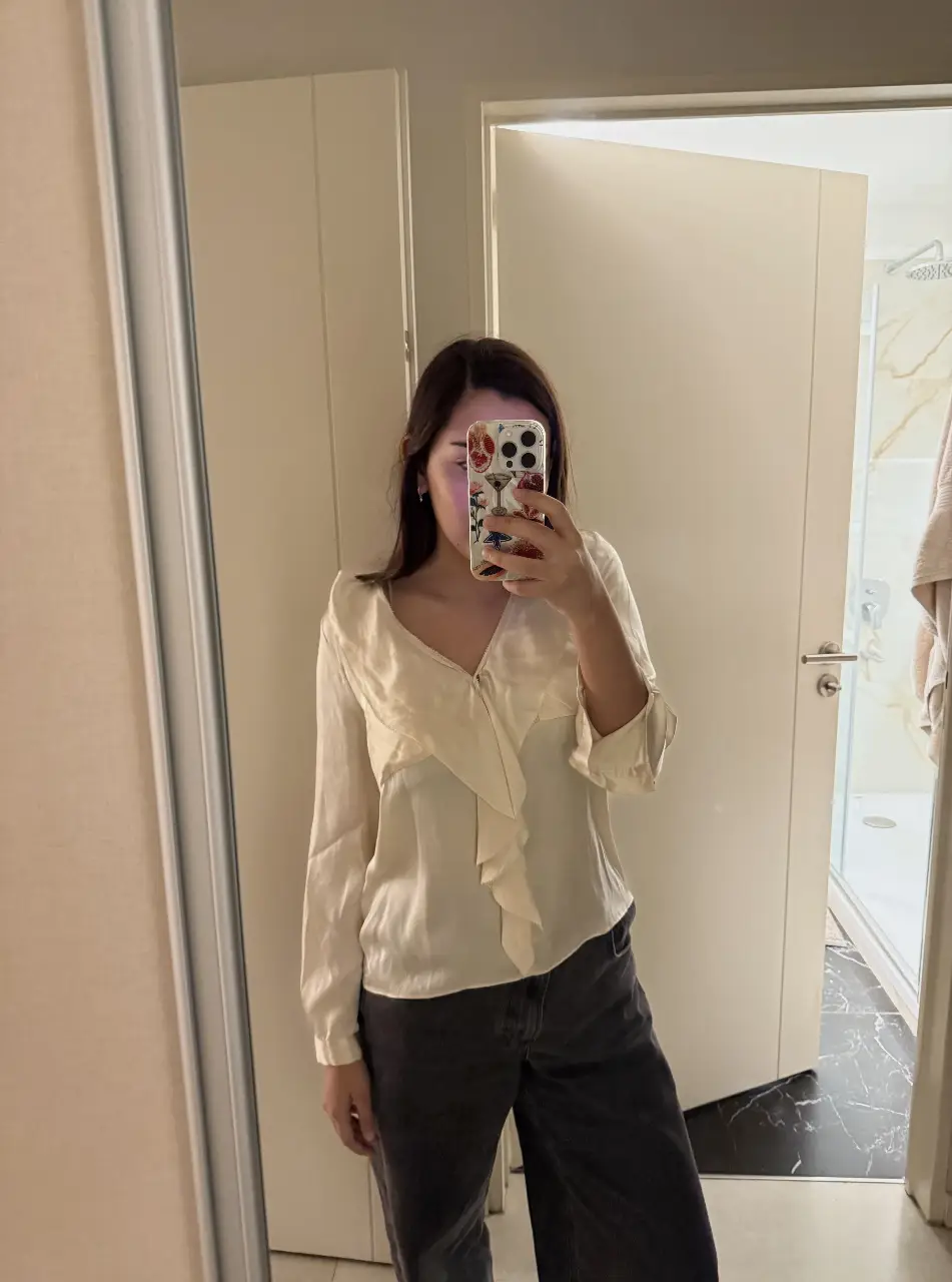 Blusa de seda color crema con detalle de volantes en el frente y mangas largas. Ideal para un look elegante y sofisticado.