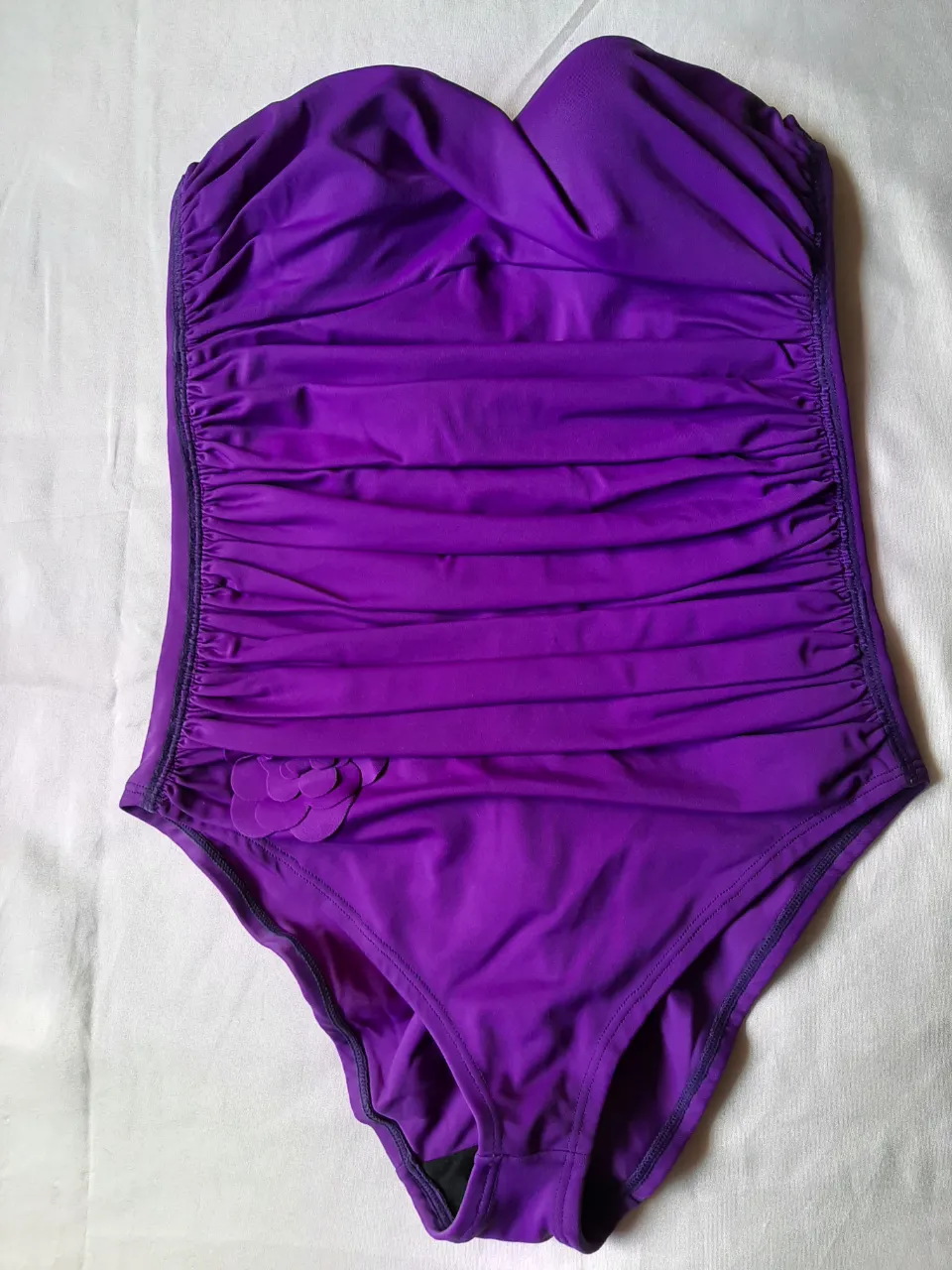 Enterito de baño color violeta, strapless, con fruncido en la parte delantera y detalle de flor en la cadera. Ideal para disfrutar de la playa o la pileta con mucho estilo.