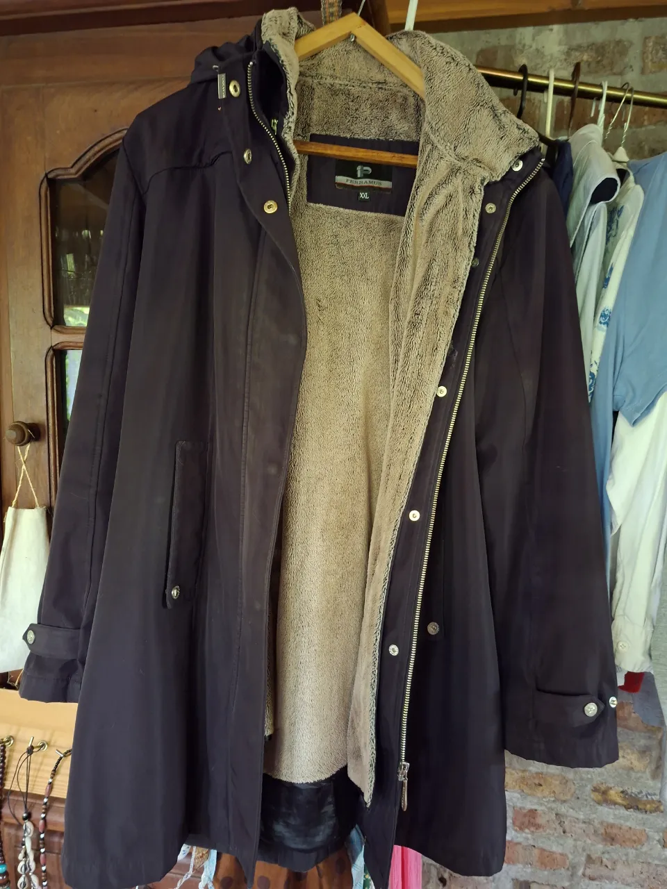 Campera larga de color azul marino con interior de peluche color beige. Posee capucha, cierre y botones a la vista. Tiene bolsillos frontales.