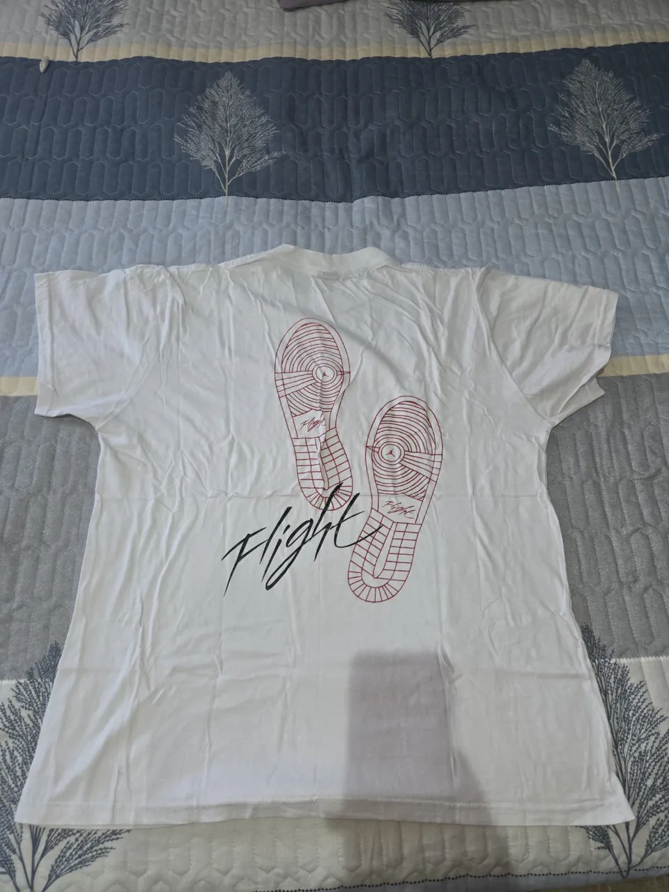 Remera blanca de manga corta con estampa de huellas de zapatillas y la palabra "Flight" en la espalda. La estampa también se repite en el frente, en menor tamaño.