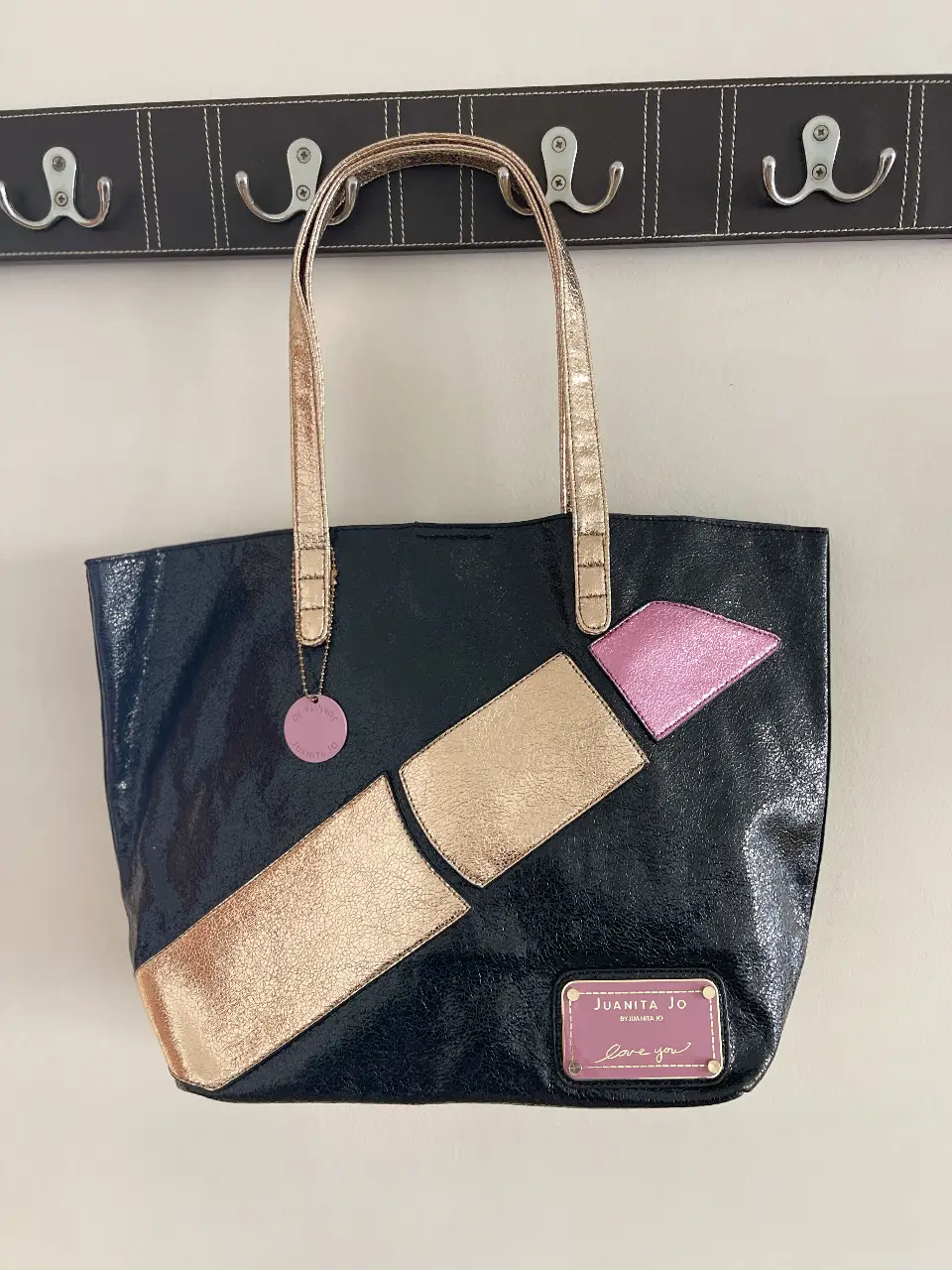 Bolso tote negro con diseño de labial dorado y rosa. Ideal para llevar todo lo necesario con estilo. Perfecto para un look casual y moderno.