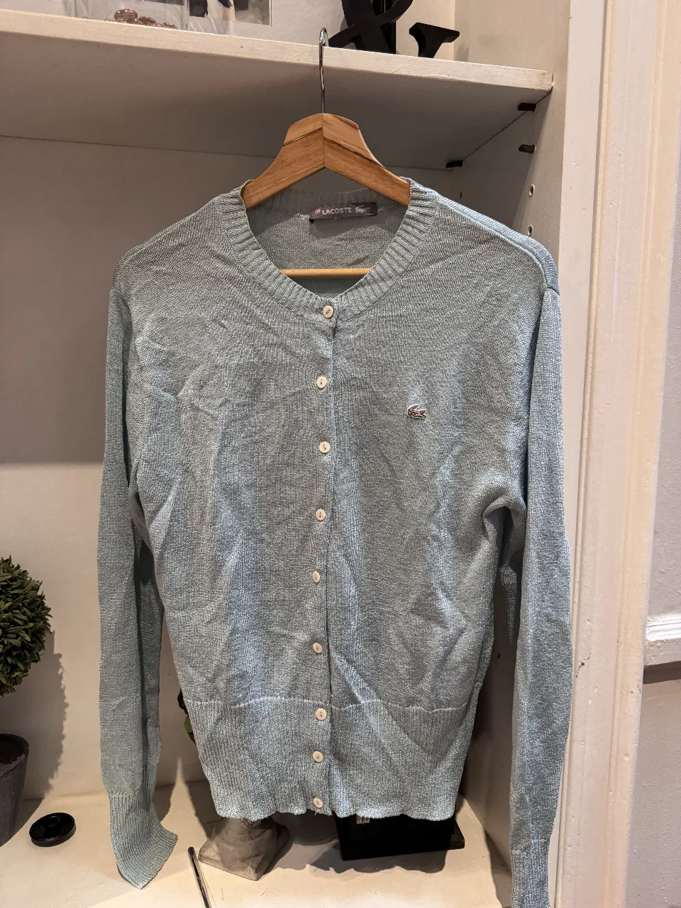 Cardigan celeste de la marca Lacoste, con botones y el logo del cocodrilo bordado. Ideal para un look casual y cómodo.