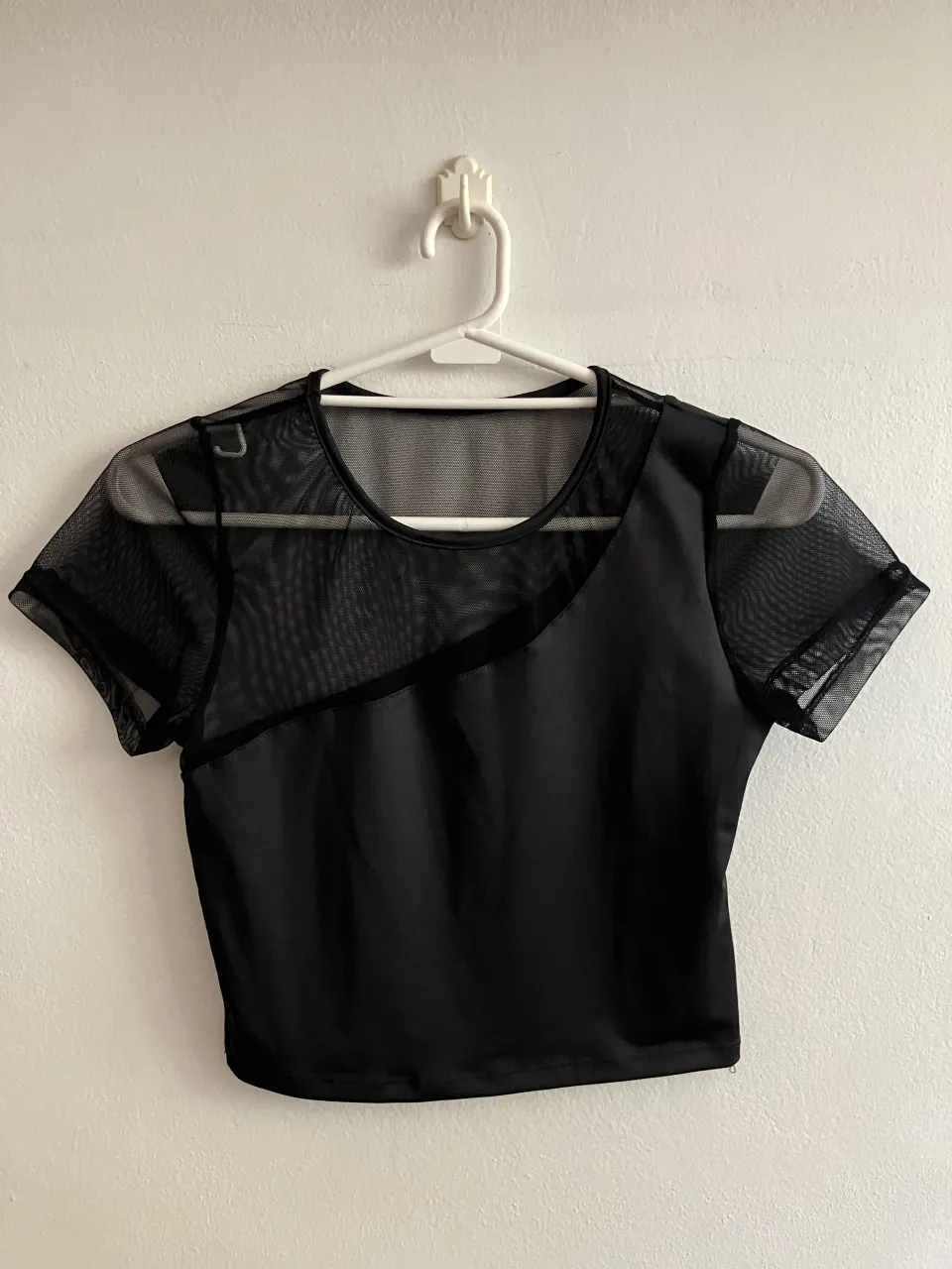 Remera negra de manga corta con detalles de mesh en la parte superior y mangas, con hombro asimétrico. Diseño moderno y canchero, ideal para un look urbano o de fiesta.