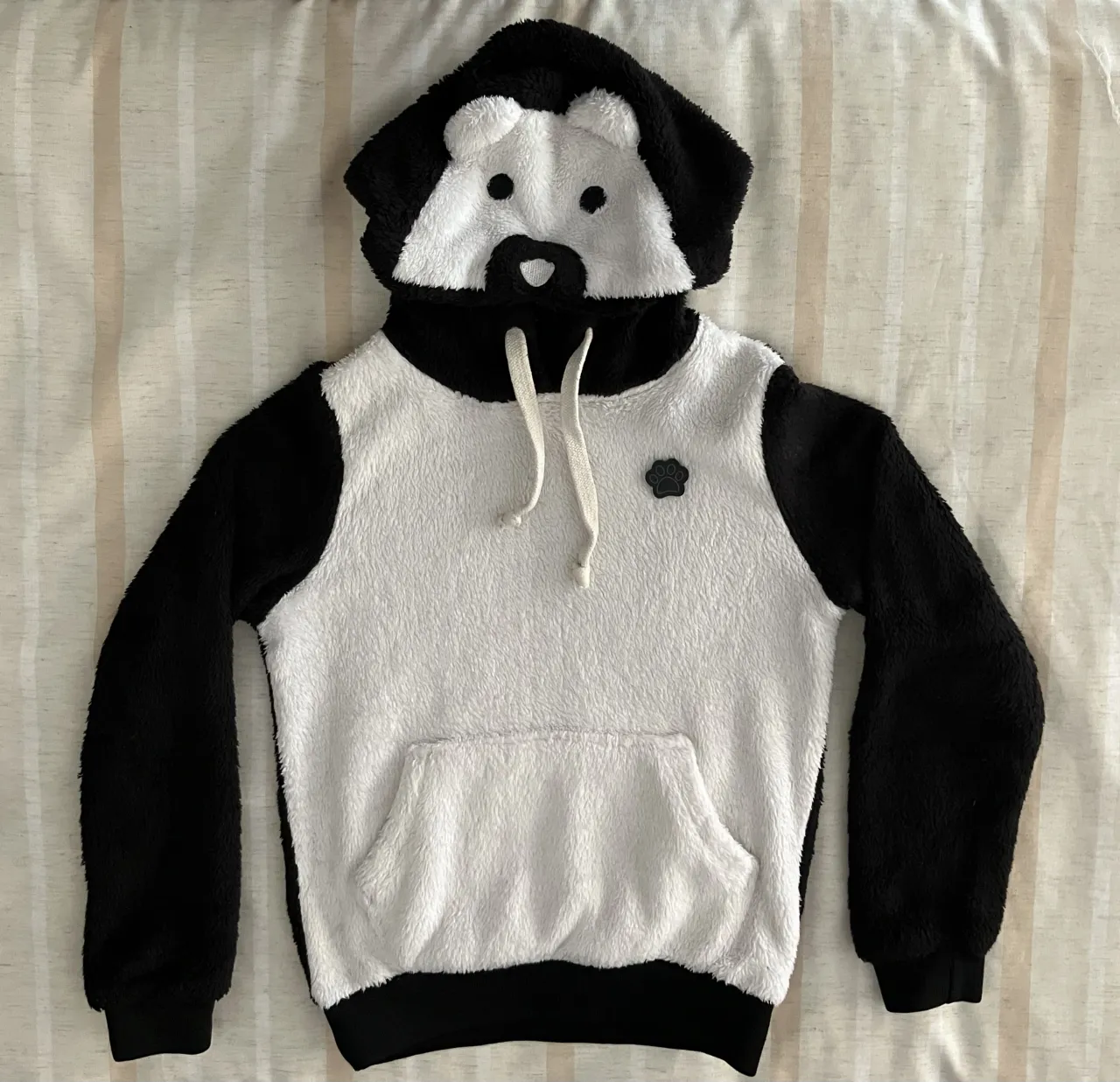 Buzo súper tierno y original con diseño de oso panda. Confeccionado en plush suave, ideal para mantenerte abrigado/a con mucho estilo. Posee capucha con detalles de orejitas y cara de oso, bolsillo canguro al frente y un pequeño pin con forma de huella, propio de la marca. El talle correspondiente en la guia de talles es 6/8.