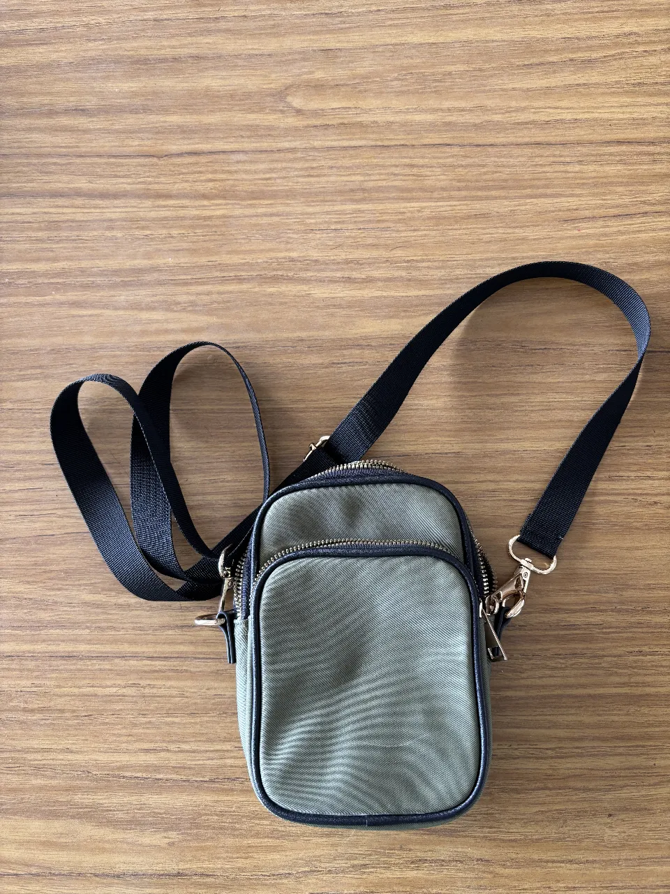 Bandolera de color verde militar con detalles en negro y cierre dorado. Ideal para llevar lo esencial con estilo y comodidad.