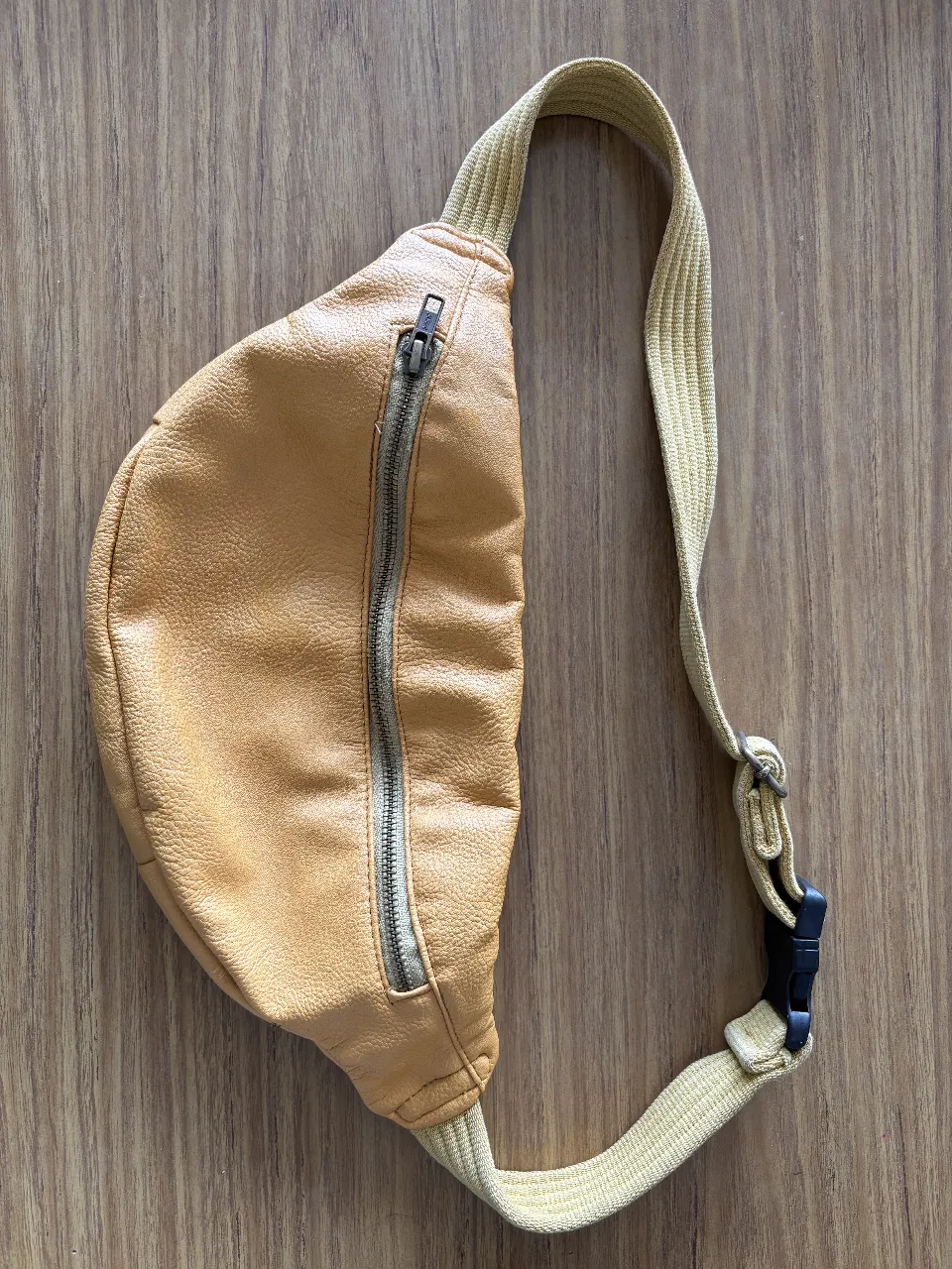 Riñonera de cuero sintético color amarillo mostaza. Cuenta con un cierre frontal y una correa ajustable. Ideal para llevar tus esenciales con estilo y comodidad.